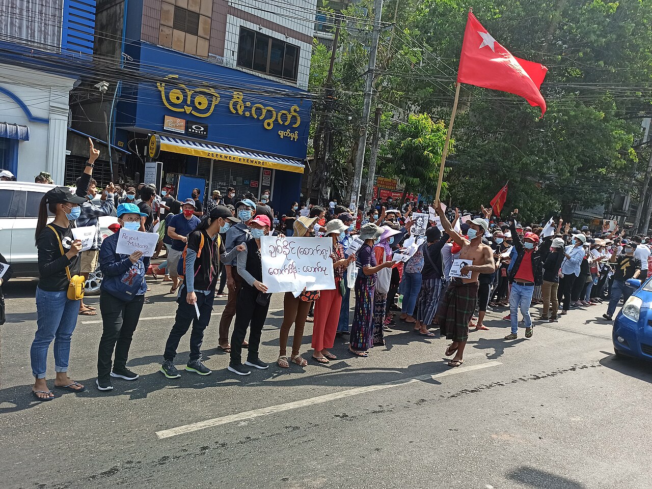 Протестиращи с червени знамена и плакати на улица в Янгон
